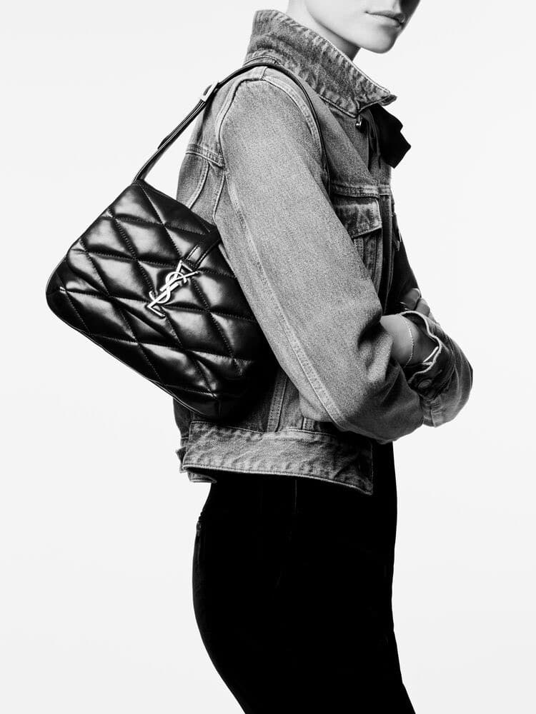 A side profile of a person wearing a denim jacket and Trendy Work Bag You Can Stylishly Wear To The Office with a metallic chain and logo. The image is in black and white, focusing on the outfit details.