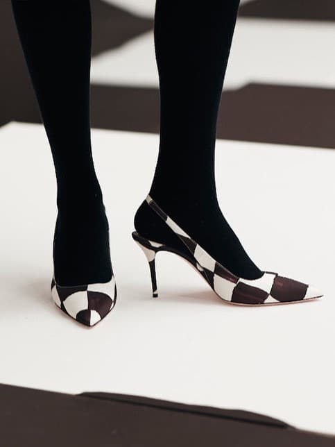 A person wearing black and white checkered We're Obsessing Over These Perfect Designer Pointed Heels stands on a beige surface, with only their feet and ankles visible.