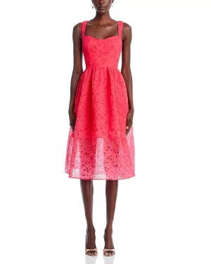 A woman stands wearing a sleeveless, FRENCH CONNECTION coral pink lace midi dress that reaches mid-calf, paired with light brown heels. The dress features a fitted bodice, square neckline, and a flared