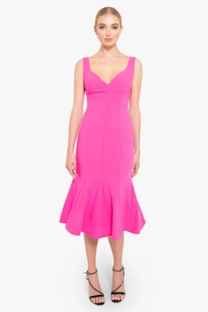 A woman wearing a bright pink Black Halo Arlott Midi Dress with a flared hem stands facing forward. She has her hair pulled back and is wearing black strappy high-heeled sandals.