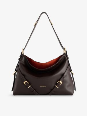 A dark brown Givenchy Voyou Small Leather Shoulder Bag with gold-tone buckles, an adjustable strap, and a slouchy design. The interior is reddish-brown, with the Givenchy logo printed in gold on the front.