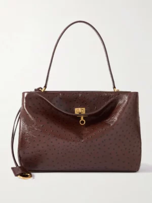 A dark brown Balenciaga Rodeo Small Croc-leather Tote with a textured, dotted pattern, single top handle, gold hardware, front clasp closure, and a matching leather tag attached by a thin strap.