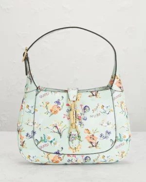 A light blue Gucci Small GG Marmont Shoulder Bag with a floral print, short strap, gold-tone hardware, and front buckle closure is displayed upright against a light-colored background.