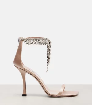 A high-heeled, open-toe sandal in nude satin with a thin front strap and a crystal-embellished ankle strap featuring dangling jewels, inspired by the elegance of Jimmy Choo Elsy 70 Snake-effect Leather Slingback Sandals.