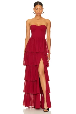 A woman stands facing forward wearing the strapless, layered Hattie Gown in dark red with a thigh-high slit. She has her hair pulled back, wears hoop earrings and black open-toe heels, set against a plain white background.