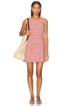 A woman stands facing forward wearing a Matteau Broderie Tie Mini Dress in red and white checks, black sandals, and holding a large beige woven tote bag over one shoulder.