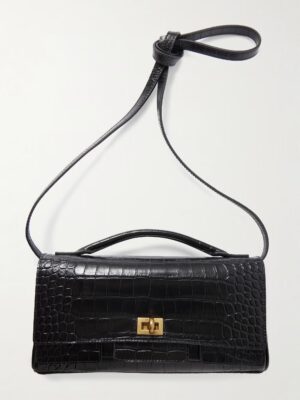 A rectangular black handbag with a crocodile-embossed texture, gold-tone clasp, short top handle, and a long shoulder strap tied in a simple knot at one end, inspired by the Balenciaga Bel Air Carry All Mini Leather Top-Handle Bag.