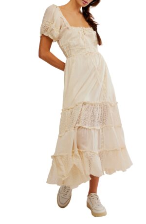 A person wearing the cream-colored Free People Alejandra Midi Dress with lace details and white sneakers. Only the lower face and body are visible; arms are relaxed at the sides.