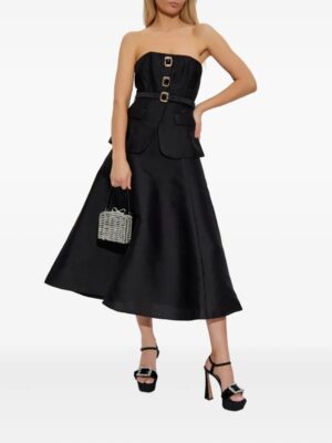 A woman wearing a strapless black midi dress with gold buckle details and pockets, reminiscent of the Self-Portrait Bow-Detail Lace Minidress, holding a small woven box handbag and pairing it with black high-heeled sandals with buckles.