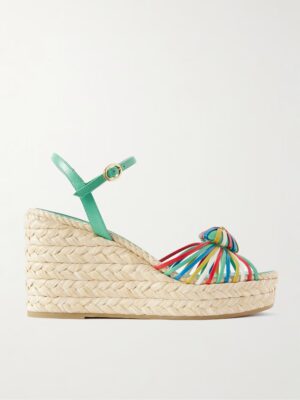 A wedge sandal with a braided straw sole, green ankle strap with buckle, and multicolored straps across the toe area evokes the chic style of Valentino Garavani Rockstud Double Denim Espadrille Sandals, set against a plain white background.