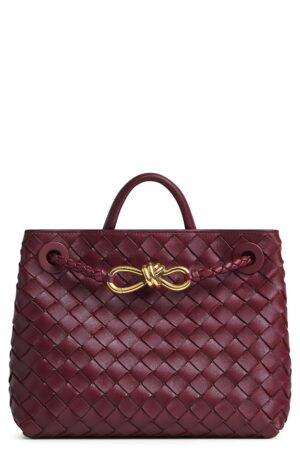 A burgundy leather tote bag with a woven pattern inspired by the Bottega Veneta Long Andiamo Intrecciato Leather Clutch, two handles, and a gold knot-shaped accent on the front.