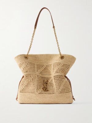 A beige woven tote bag with a gold chain and brown leather shoulder strap, featuring a gold YSL logo charm on the front and grommet details at the top edges, inspired by the Saint Laurent Jamie Cassandre Large Suede Shoulder Bag.