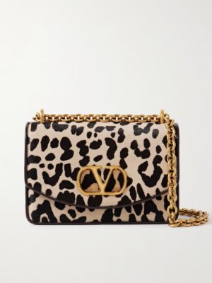 A rectangular handbag with a black and beige leopard print pattern, a gold chain strap, and a prominent gold "V" logo on the front flap inspired by the iconic Valentino Garavani Locò Small Embellished Metallic Leather Shoulder Bag.