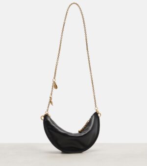 A black crescent-shaped handbag, inspired by the Chloé Spin Leather Tote, features a gold chain strap and elegant gold charms, displayed upright on a light surface against a plain white background.