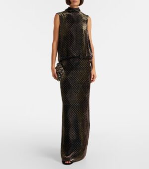 A person stands wearing a sleeveless, floor-length dress with a high neckline and loose, blouson top—reminiscent of a Dries Van Noten Denim Midi Dress. The dark background features a small polka dot pattern. The person holds a small, textured clutch.