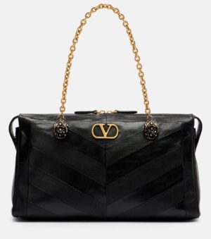 A Valentino Garavani Growl Medium Embellished Leather Shoulder Bag featuring black chevron-patterned leather, a gold chain strap with two round accents, a gold logo clasp, all set against a plain light background.