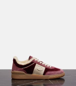 A burgundy and beige corduroy sneaker by Upvillage, featuring cream laces, a rubber sole, and cozy shearling lining, displayed on a dark marble surface against a plain light background.