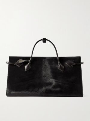 A rectangular black Alaïa Le Teckel Large Leather-trimmed Calf Hair Tote with smooth, shiny leather, two handles, a small metal logo plate on the upper left side, and minimalistic detailing against a plain background.