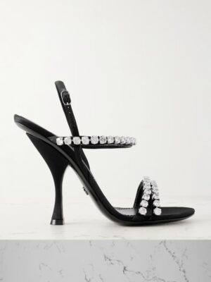 A black Dolce & Gabbana Crystal-embellished Satin Sandal with an unusual flared heel and two rhinestone-adorned straps is displayed on a white marble surface against a plain background.