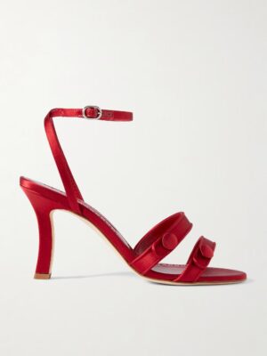 A red high-heeled sandal, inspired by the Manolo Blahnik Neusita 90 Satin Sandals, with an ankle strap and buckle, two front straps with round button details, and a mid-height heel, displayed against a plain white background.