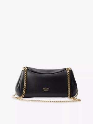 A black Prada Bonnie Leather Tote Bag with gold chain straps and the Prada logo printed in gold on the front, placed against a plain white background.