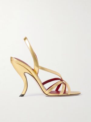 A gold, high-heeled sandal with a curved heel, open toe, thin cross-over straps, and an ankle strap. The red insole adds a bold touch. Displayed against a plain background, this look echoes the Valentino Garavani Fetishique 105 Metallic Leather Slingback Sandals.
