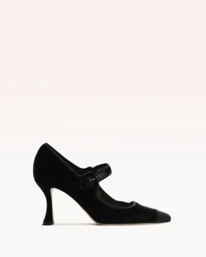 A black suede Mary Jane inspired by the Alexandre Birman Clarita Bell Slingback 60, featuring a rounded toe, buttoned strap across the instep, and a medium-height flared heel, set against a white and pale pink background.