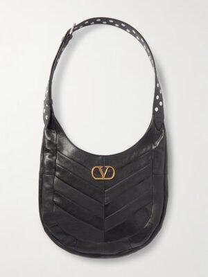 A black leather Valentino Garavani Studded Medium Leather Shoulder Bag with chevron stitching, a gold-tone V-logo on the front, and a wide shoulder strap featuring a white polka dot pattern.