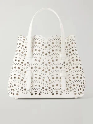 A white Alaia Mina 20 Laser-cut Leather Tote with two handles, featuring an intricate cutout pattern of scalloped edges and geometric shapes, displayed against a plain light background.