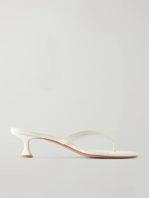 A minimalist white heeled sandal inspired by the AMINA MUADDI Alexa Corded Lace and Leather Pumps, featuring a thin thong strap and a low, flared heel, displayed against a plain light gray background.