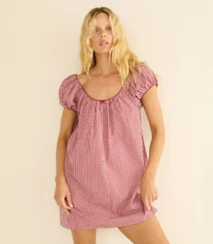 A woman with long blonde hair wears a short-sleeved, red and white gingham Dôen Julia Dress with a scoop neckline. She stands against a plain, light-colored background, looking directly at the camera.