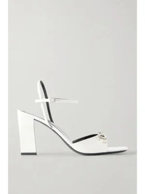 A white heeled sandal inspired by Gucci Signora Horsebit-embellished Patent-leather Sandals, featuring an open toe, ankle strap with a silver buckle detail, a block heel, and minimalist design, photographed against a plain light background.