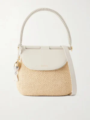 A woven beige Loewe + Paul Ibiza Pescador Leather-trimmed Raffia Shoulder Bag features a white leather flap, braided top handle, detachable strap, and a metallic fish-shaped charm. The brand "Loewe" is embossed on the flap.