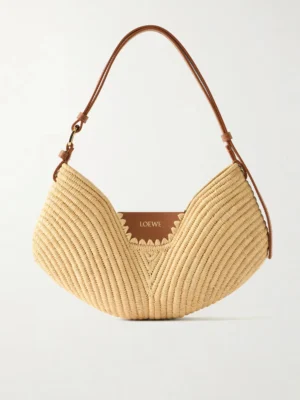 The Loewe + Paul Ibiza Swing Leather-trimmed Raffia Shoulder Bag features a beige woven raffia body, curved shape, brown leather adjustable strap, and an interior leather patch stamped with “LOEWE.”.